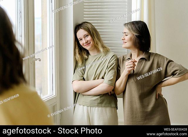 Smiling mother looking at daughter leaning on wall