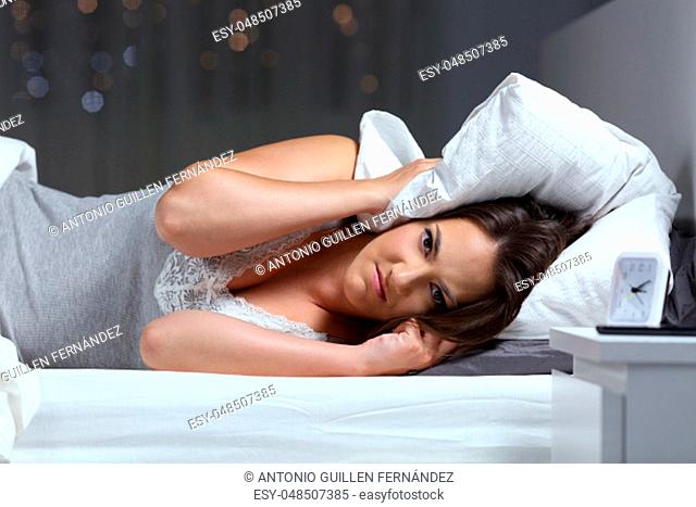 Angry woman suffering for neighbour noise and looking at camera lying on a bed in the night at home