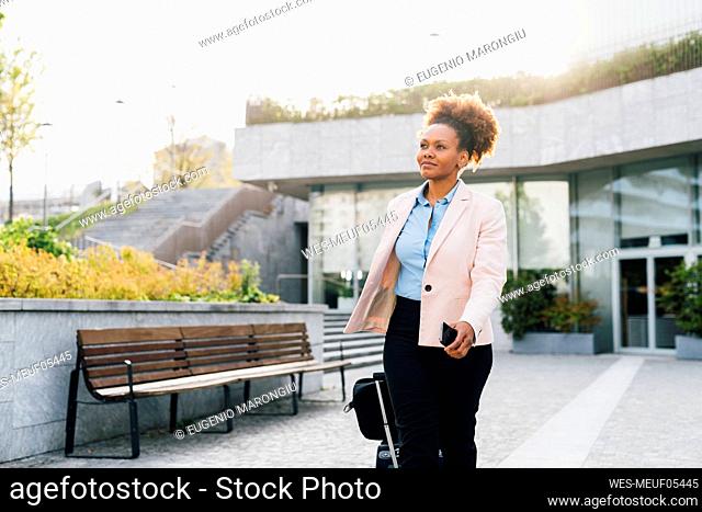 Smiling businesswoman walking with luggage