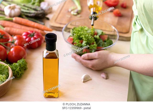 Preparing salad with rapeseed oil, lettuce, tomatoes, carrot, garlic, asparagus