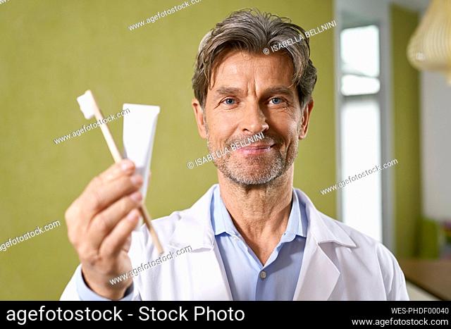 Portrait of dentist holding toothbrush and toothpaste in his medical practice