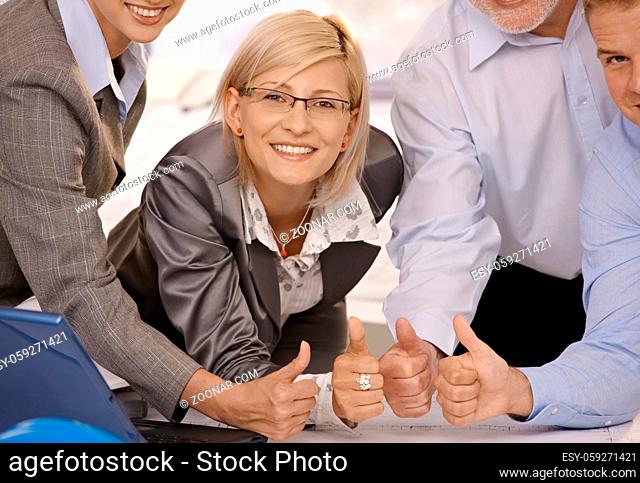 Smiling confident businesswoman giving thumbs up with team in office