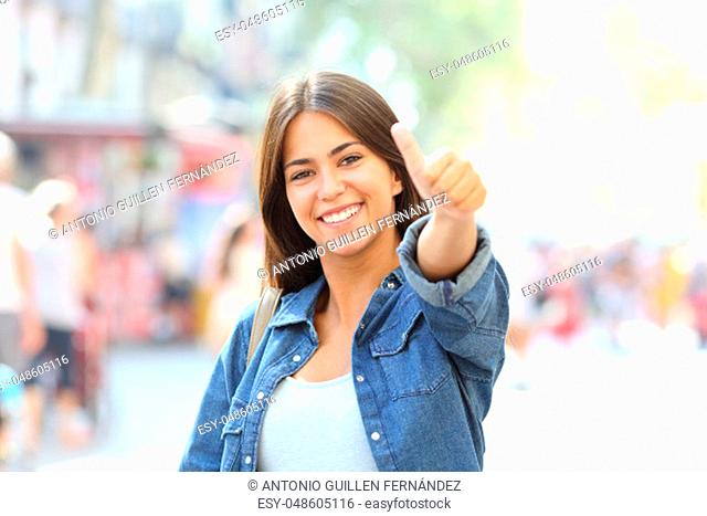 Happy girl posing with thumb up looking at camera in the street
