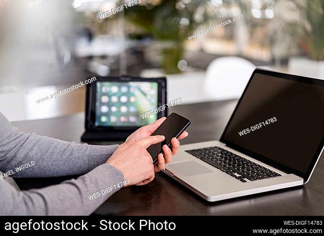 Businessman's hands using smart phone by laptop at office