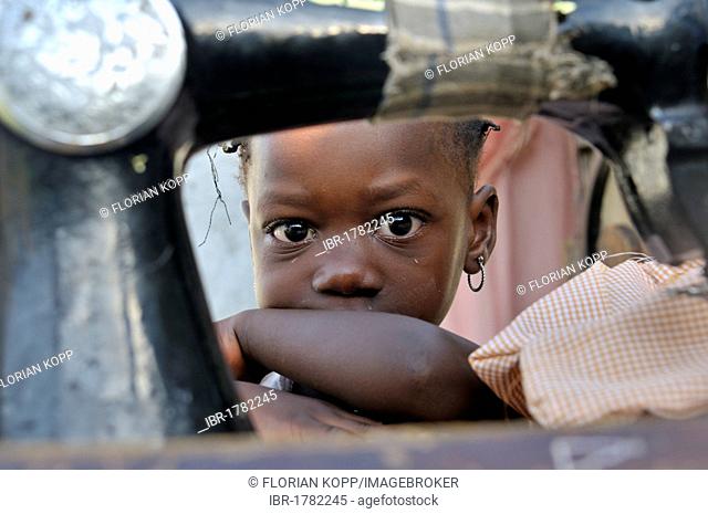 Little girl hiding behind an old mechanical sewing machine, camp for victims of the January 2010 earthquake, Croix-des-Bouquets district, Port-au-Prince, Haiti