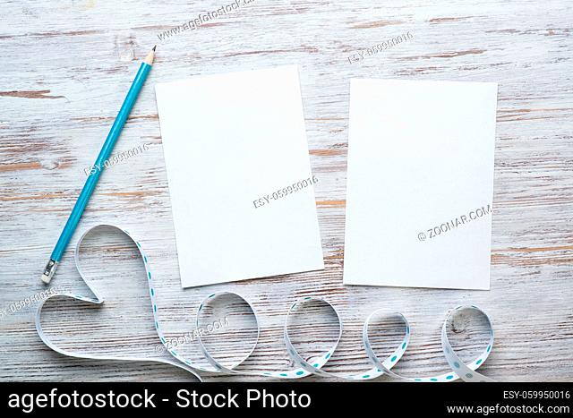 Flat lay cute composition with ribbon in shape of heart. Blank sheet of white paper on vintage wooden table. Declaration of love letter