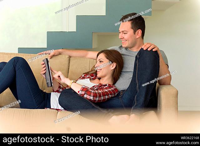 Young couple relaxing at luxurious home with tablet computers reading in the living room on the sofa couch