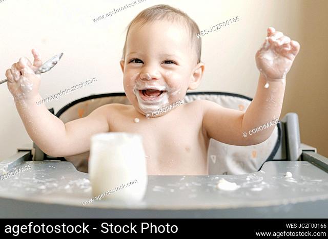Little baby boy eating yogurt in highchair at home