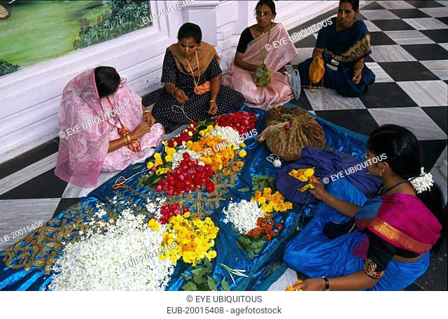 Women wearing colourful saris making flower garlands, sitting on black and white checked floor