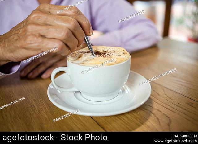Close up of woman stirring coffee while sitting at table in cafe || Model approval available