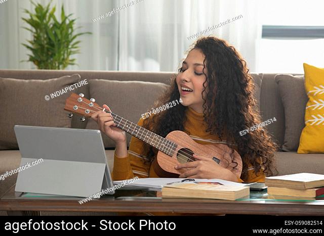 A TEENAGE GIRL SITTING AND PLAYING UKELELE AT HOME