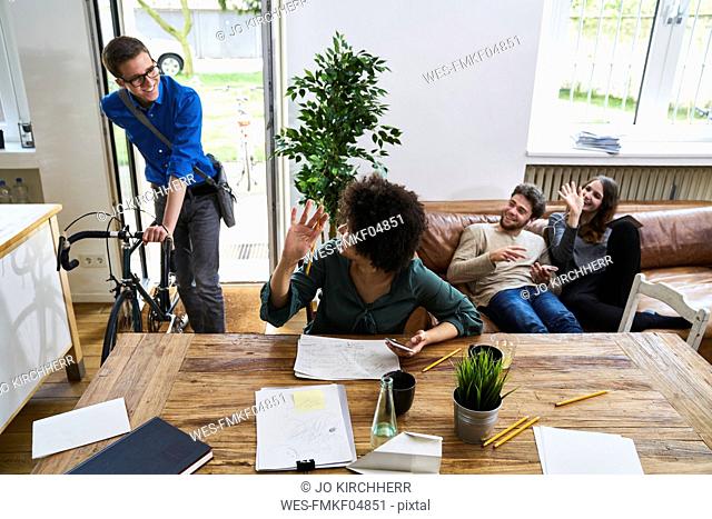 Coworkers waving at young man with bicycle arriving in modern office