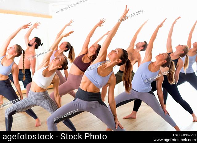 Group of young authentic sporty attractive people in yoga studio, practicing yoga lesson with instructor. Healthy active lifestyle, working out in gym