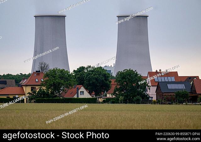 30 June 2022, Saxony-Anhalt, Leuna: Single-family homes stand in front of the distinctive cooling towers of the refinery in Leuna
