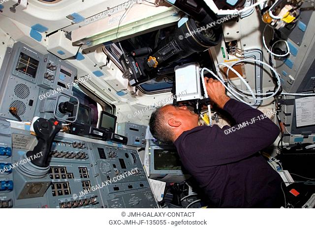 Astronaut John Danny Olivas, STS-117 mission specialist, aims a laser range finder through one of the overhead windows on the aft flight deck of the Space...