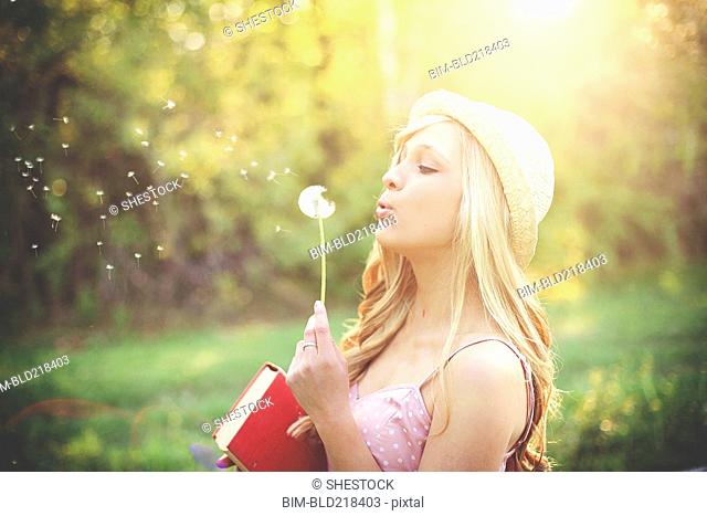 Woman blowing dandelion seeds in rural field