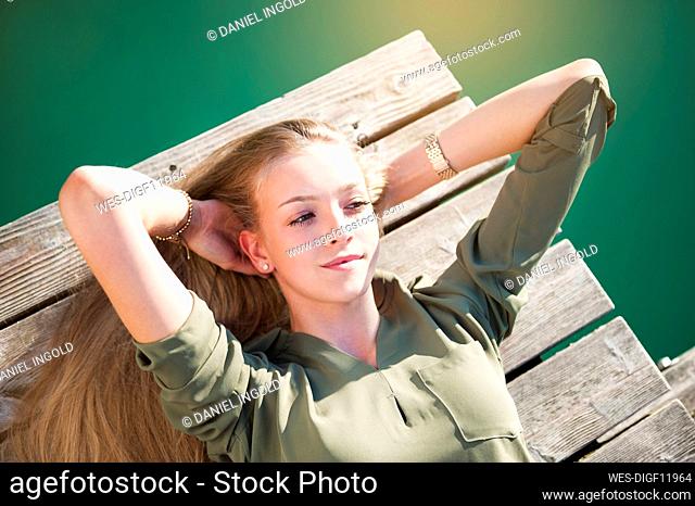 Portrait of young woman with hands behind head lying on jetty at lake