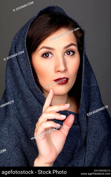 Beauty portrait of brunette woman dressed in dark blue scarf. Female portrait from a three-quarter angle on black background. Hand in front of face