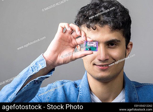 Young man holding a USB connectivity for standard SD memory cards with right hand in front of his face
