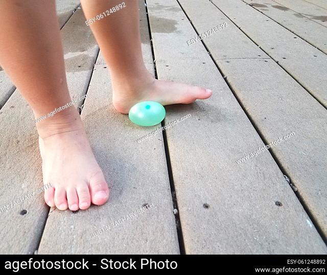 child's foot on water balloon trying to pop it on deck