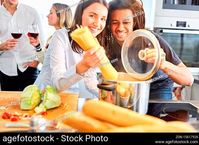 Glückliche Freunde oder Paar beim Spaghetti Nudeln kochen in WG Küche am Herd