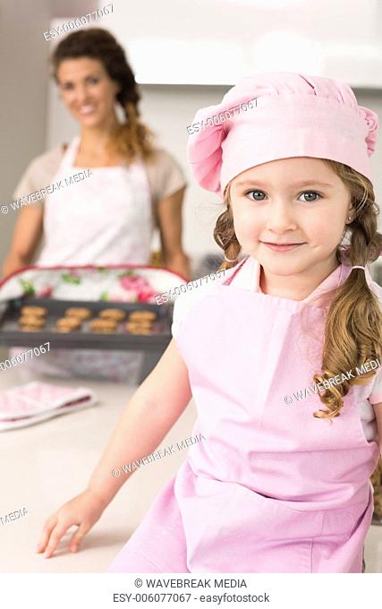Cute girl wearing pink apron and chefs hat smiling at camera
