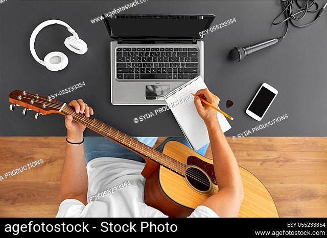 man with guitar writing to music book at table