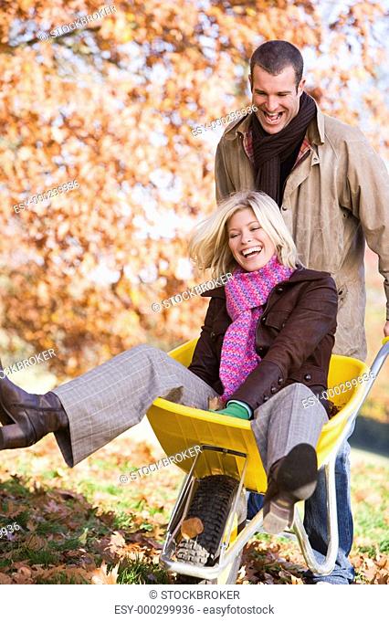 Man outdoors pushing woman in wheelbarrow and smiling selective focus