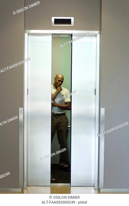 Young man standing in elevator with hand under chin, doors closing
