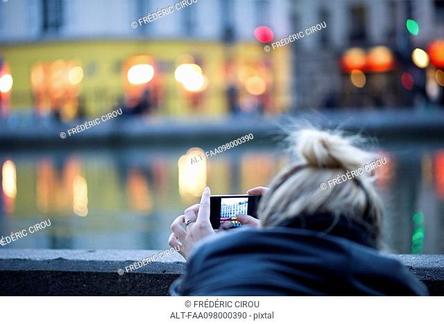 Woman using smartphone to photograph city scene