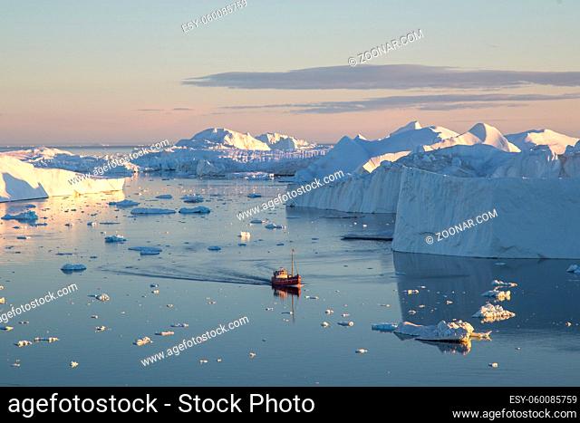 Ilulissat, Greenland - July 7, 2018: A red fishing boat sailing in between icebergs on Ilulissat Icefjord