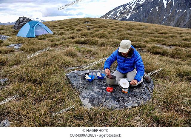 Mid adult woman cooking food on camping stove, New Zealand