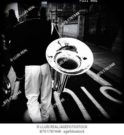 musico de espaldas caminando por la calle con una tuba en la mano, musician view from the back walking down the street with a tuba in the hand