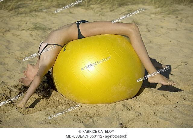 Young girl playing with a big yellow balloon on the sand beach