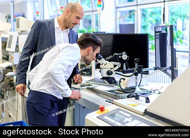 Young engineer looking through microscope while standing by businessman at laboratory
