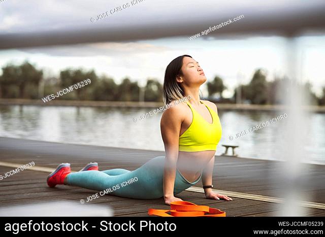 Active woman doing cobra stretch with eyes closed on jetty