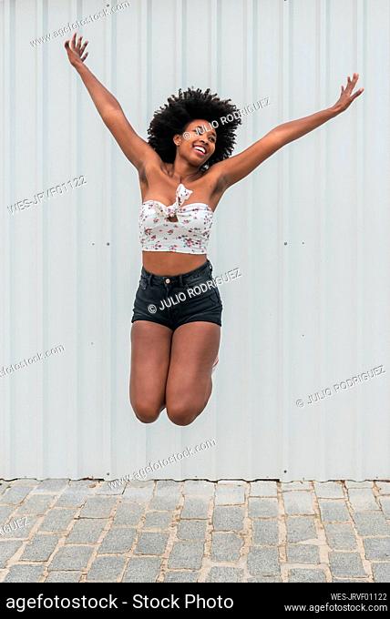 Carefree woman with arms raised jumping on footpath