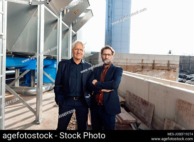 Smiling senior businessman standing with colleague at industrial building