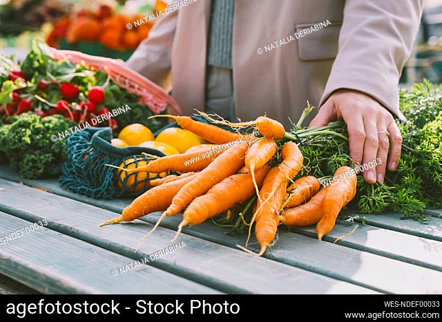Hands of woman on bunch of carrots at table