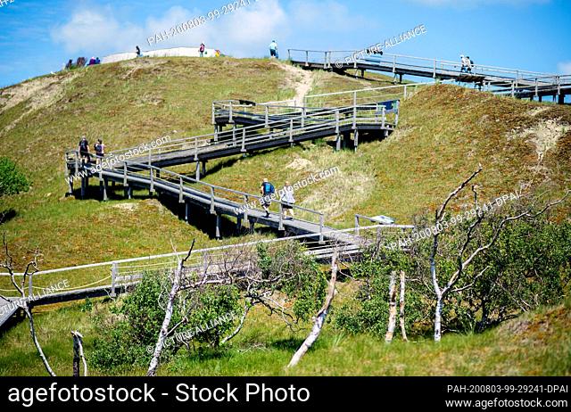 12 July 2020, Lower Saxony, Norderney: Tourists walk up a wooden staircase to the Thalasso platform, a viewing platform located in the dunes