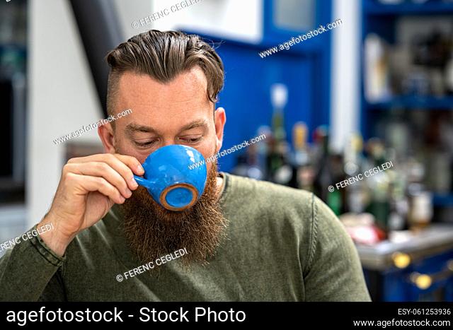 Dark tonal close up portrait of a young stylish handsome bearded Canadian man enjoying coffee in a country bar