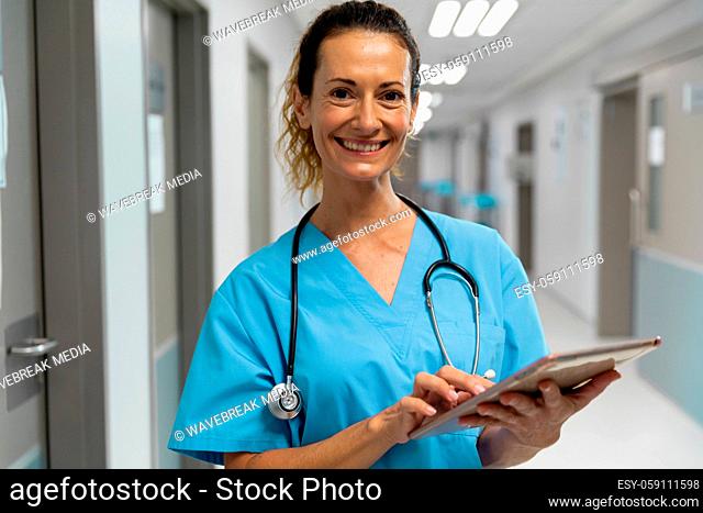 Portrait of mixed race female doctor stading on corridor smiling using laptop