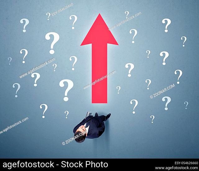 Young contemplating businessman stands in front of a big red arrow and white question marks