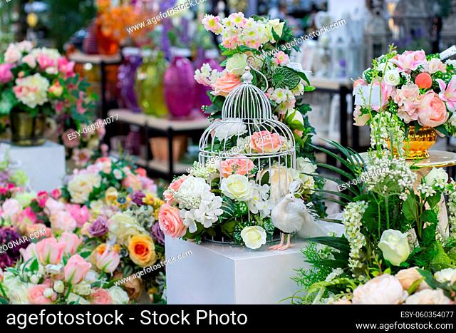 A flower arrangement of artificial roses, a metal birdcage and a fabulous white bird. Home interior decoration, textile rose flower pink white with green leaves