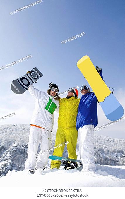 Portrait of three successful snowboarders raising their arms on mountain top