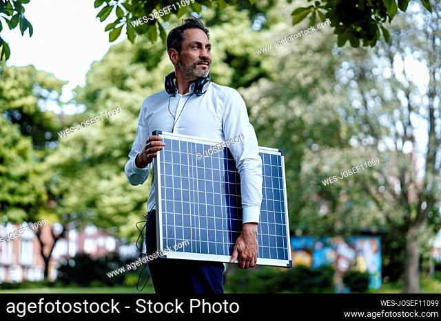 Mature businessman holding solar panel in park