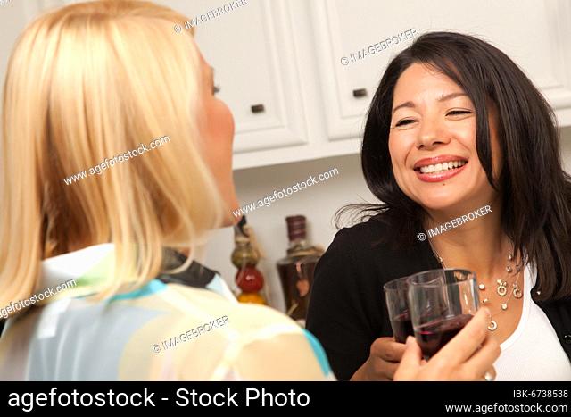 Two girlfriends enjoy a glass of wine in the kitchen