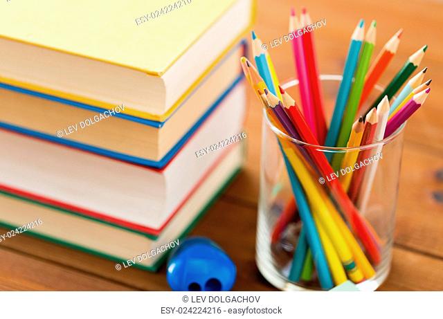 education, school, drawing, creativity and object concept - close up of crayons or color pencils with books and sharpener on wooden table