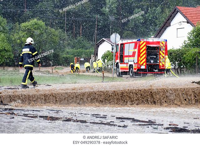 Red fire brigade engine, firefighting truck and firefighters rush to rescue when floods hit village in Europe after heavy rain, severe weather, rescue services