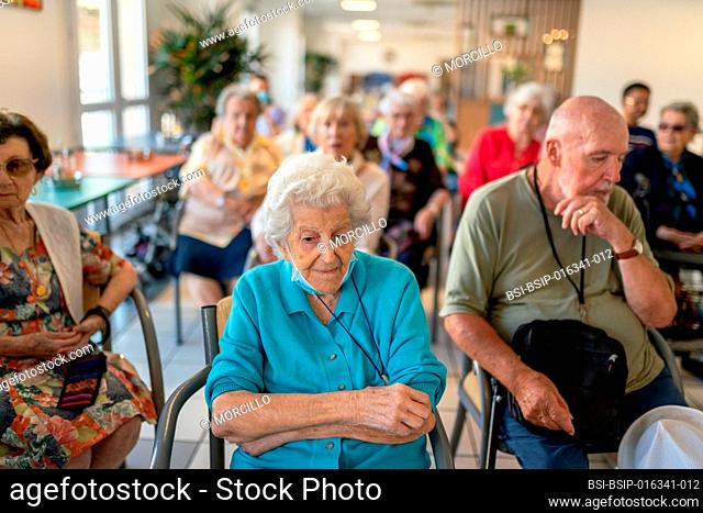 Seniors sitting in chairs or wheelchairs attending a music concert in a retirement home